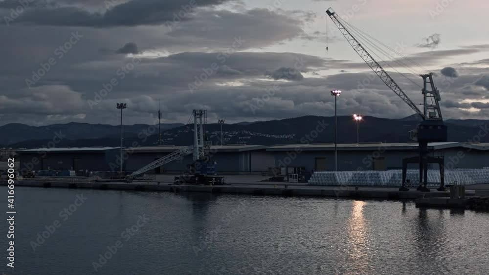 A port harbour and a crane at sunset under grey clouds, wide shot A port harbour and a crane at sunset under grey clouds, wide shot