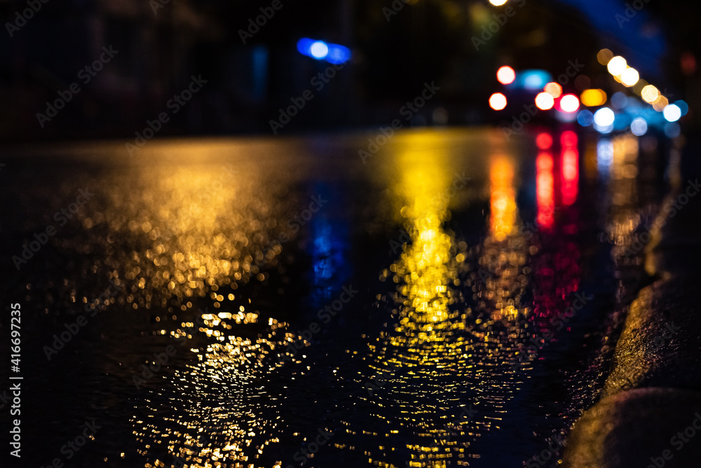 Blurred focus of a freeway during night rain with multicolored out-of-focus lights in the background. Water from the rain and the reflection of lanterns in the city