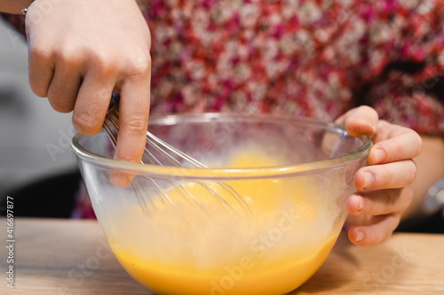 the child prepares food. whipped eggs in a clear bowl, baby hands and a whisk close-up. cooking scramble or pancake dough in your home kitchen