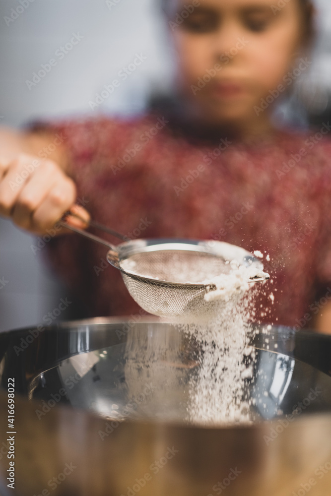 a child prepares food, a girl sifts flour through a sieve over a bowl of dough. focus on the screen, blurry girl. king breakfast at home a child prepares food, a girl sifts flour through a sieve over a bowl of dough. focus on the screen, blurry girl. king breakfast at home