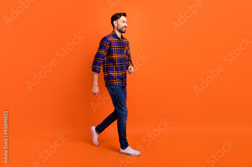 Full length profile portrait of cheerful person walking look empty space toothy smile isolated on orange color background