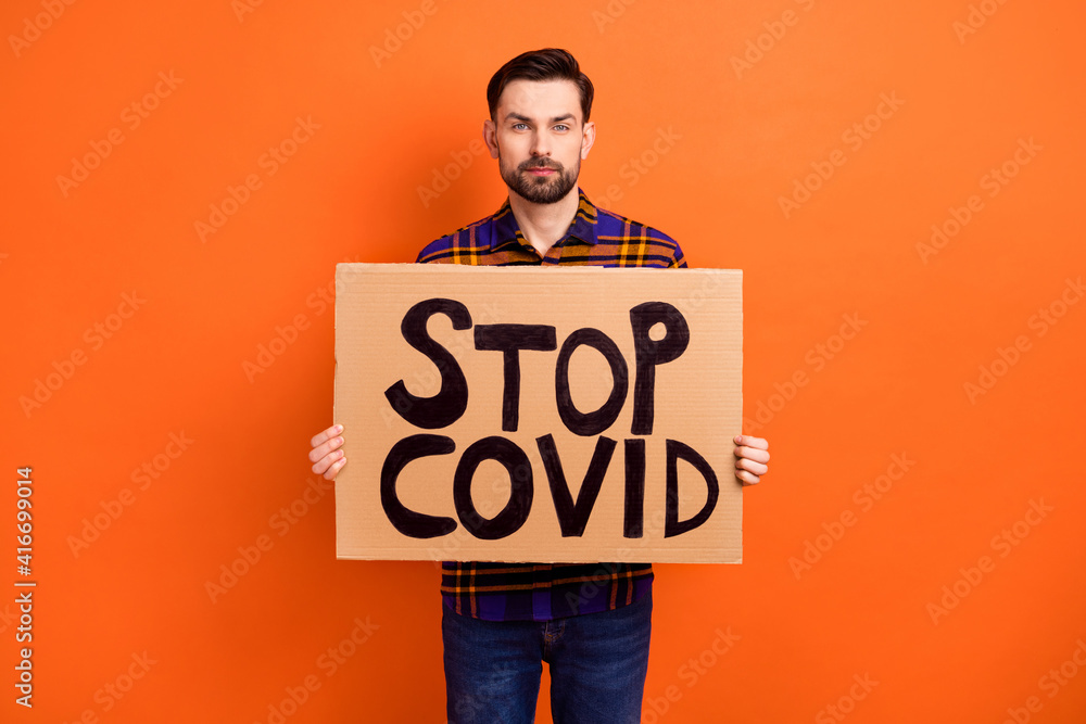 Portrait of young person hands hold paper stop covid placard look camera isolated on orange color background Portrait of young person hands hold paper stop covid placard look camera isolated on orange color background