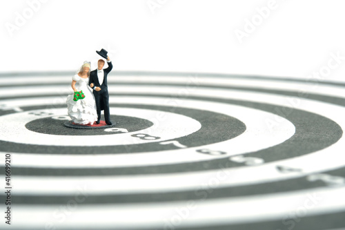 Wedding married target goal conceptual miniature people toy photography. Bride and groom standing above dartboard. Image photo