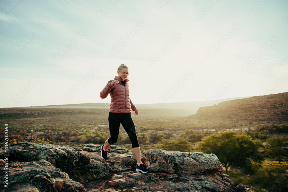 Caucasian female running in mountain along hiking trail skipping down rocks during sunset Caucasian female running in mountain along hiking trail skipping down rocks during sunset