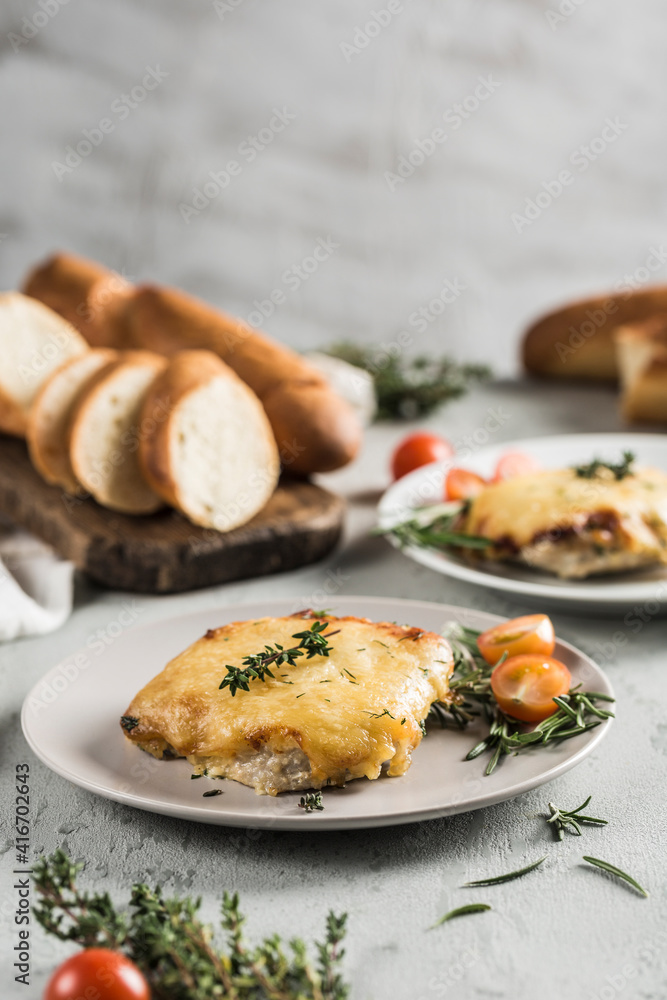 Baked meat and cheese on a plate with French bread baguette with herbs and cherry tomatoes on a light background. Baked meat and cheese on a plate with French bread baguette with herbs and cherry tomatoes on a light background.