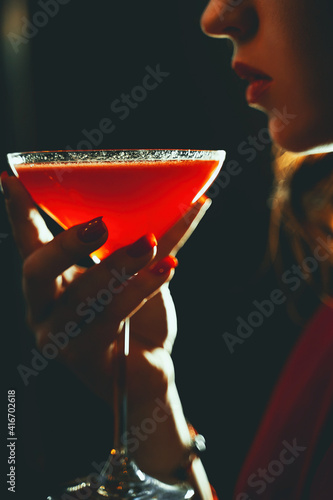 Beautiful attractive woman with red cocktail in a dark room close up