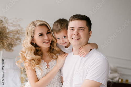 Beautiful young family man woman and son in white clothes play on the bed at home