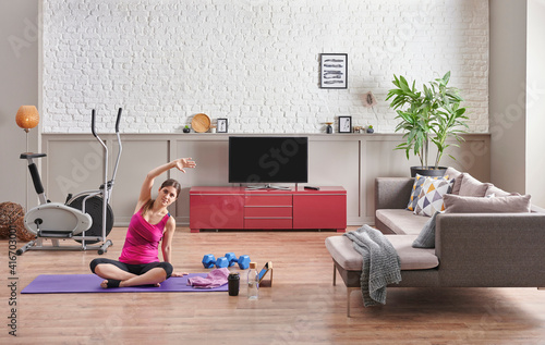 Sportive woman is doing yoga at home, purple mat, blue dumbbell, decorative living room concept. Healthy lifestyle.