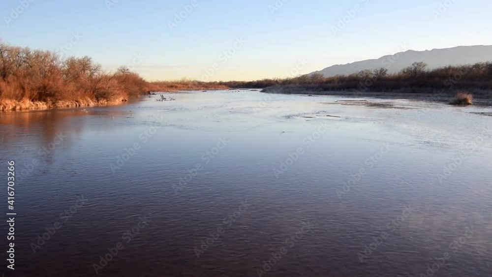 Floating in balloon across river in new mexico with morning sun peaking over horizon onto bank. Floating in balloon across river in new mexico with morning sun peaking over horizon onto bank.