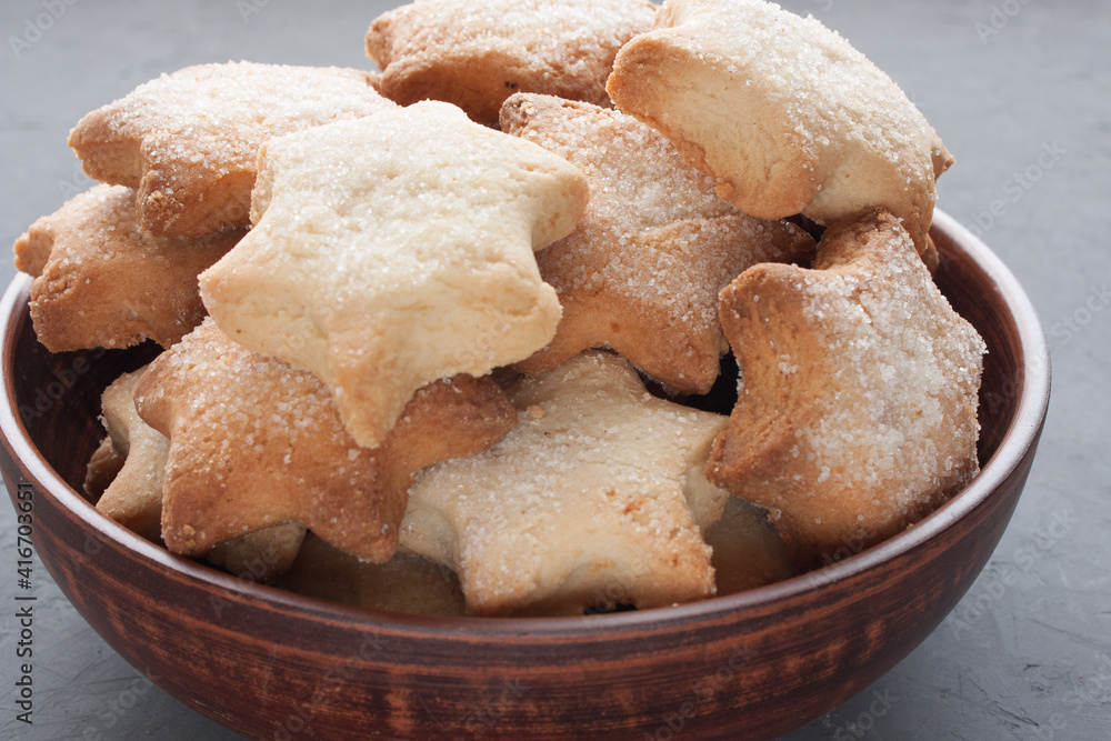 Delicious homemade cookies in the shape of stars sprinkled with sugar. It is laid out in a clay bowl on a dark gray background. Delicious homemade cookies in the shape of stars sprinkled with sugar. It is laid out in a clay bowl on a dark gray background.