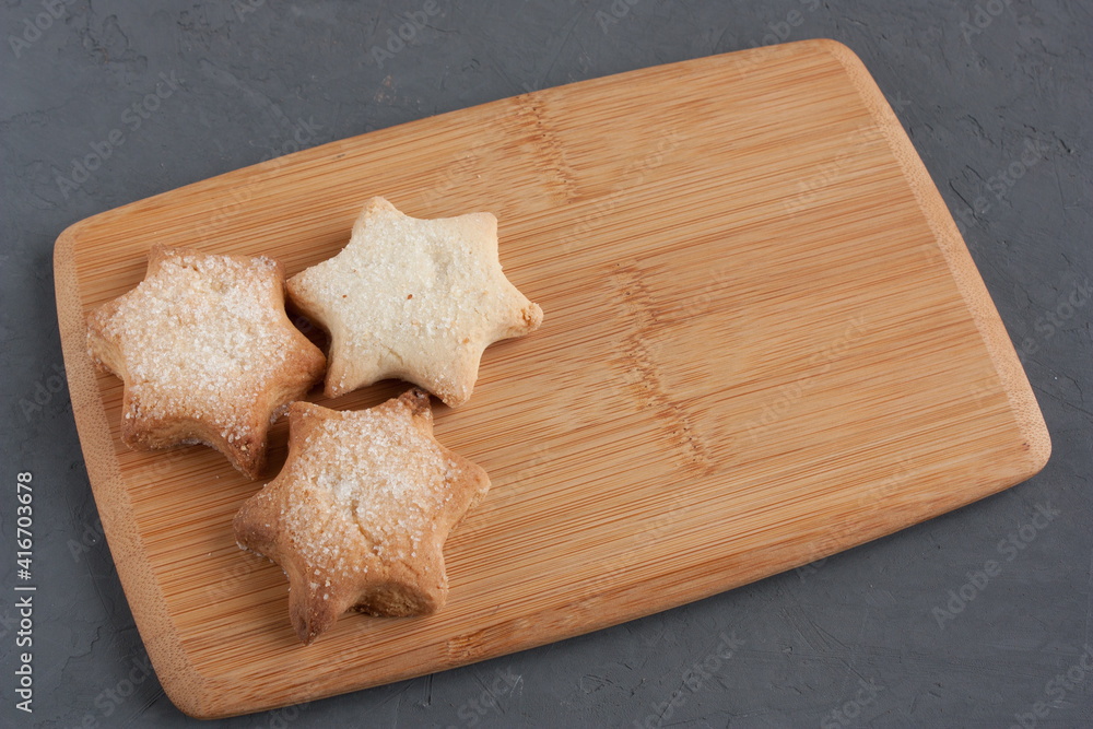 Fototapeta premium Delicious homemade cookies in the shape of stars sprinkled with sugar. Laid out on a kitchen board on a dark gray background.