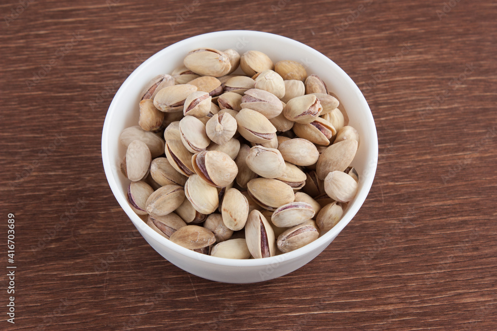 Fried salted pistachios in a white bowl on a wooden table Fried salted pistachios in a white bowl on a wooden table