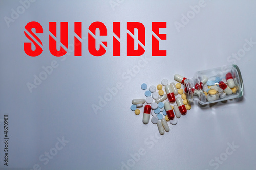 Suicide concept. White, red, blue and yellow pills and capsules come out of a transparent bottle. In large letters the word "suicide" is wrote in English.