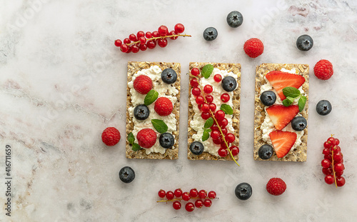 Snack with rye oats crispbread, cottage cheese, and fresh berries on a marble table.