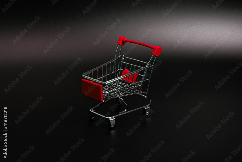 Small red shopping cart on a black background. Copspace