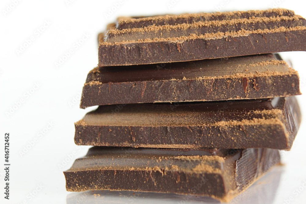 Dark bitter chocolate pieces stacked slide lies on a white background with a reflection with a place for text and copyspace Dark bitter chocolate pieces stacked slide lies on a white background with a reflection with a place for text and copyspace