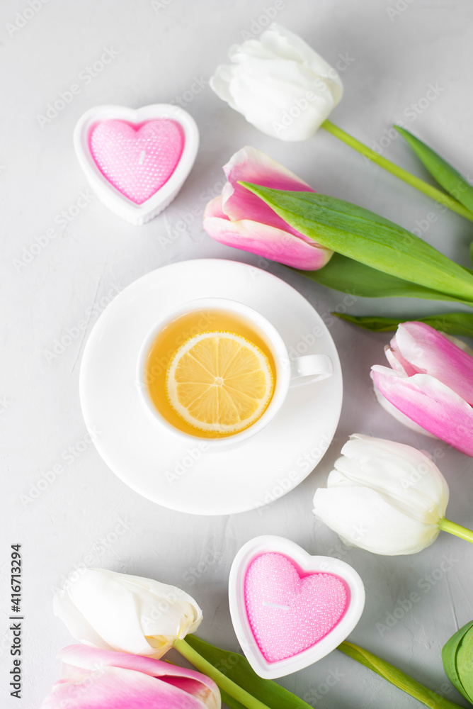 Tulips with white cup of tea on light background. Spring tenderness still life composition with candles. Flowers for romantic, love atmosphere. Relax, meditation pause. Greeting card