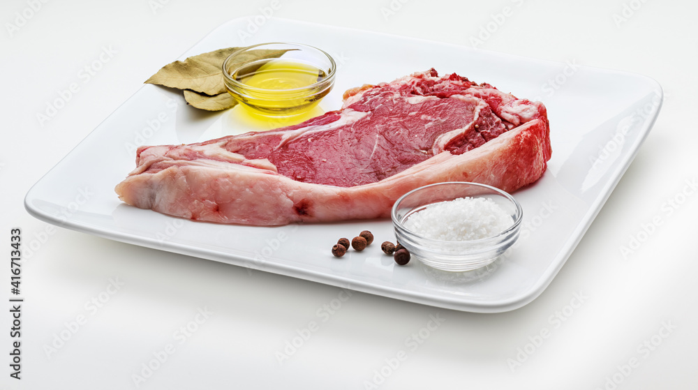 Raw red beef cutlet (beef, heifer, veal) on a plate with salt, pepper and oil. Isolated on white background.
