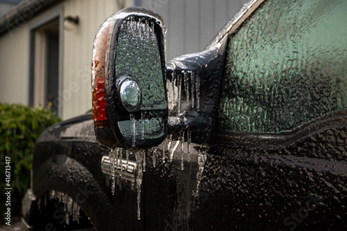 An icy-covered vehicle mirror and other parts of car after an ice storm