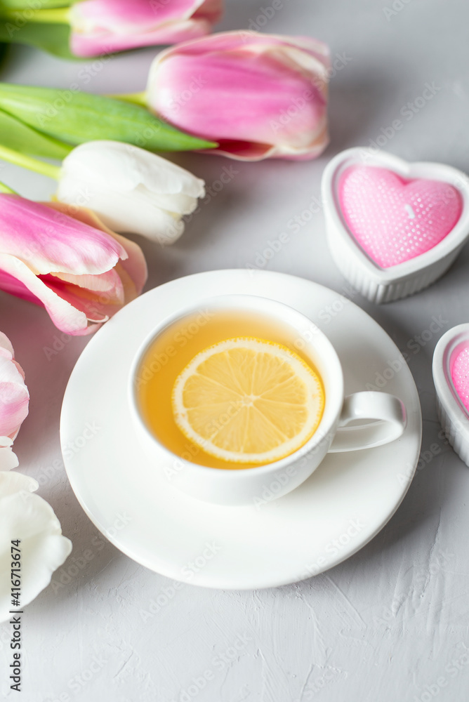 Tulips with white cup of tea on light background. Spring tenderness still life composition with candles. Flowers for romantic, love atmosphere. Relax, meditation pause. Greeting card Tulips with white cup of tea on light background. Spring tenderness still life composition with candles. Flowers for romantic, love atmosphere. Relax, meditation pause. Greeting card