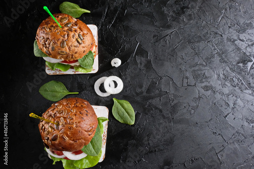 Vegetarian hamburger with tomato, lettuce, onion, bean cutlet and grain bun on dark  background. It  is an alternative to the usual hamburger.  The concept of healthy eating.Copy space. Top view.