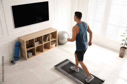 Sporty man training on walking treadmill while watching TV at home