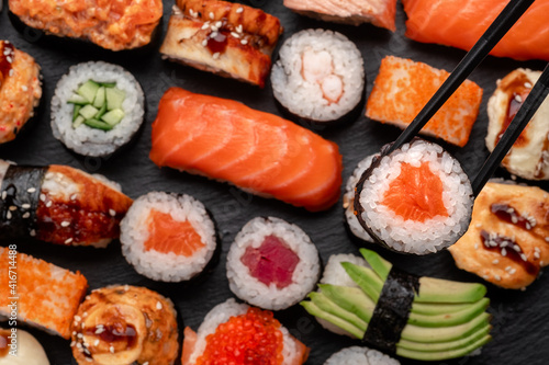 Assorted sushi nigiri and maki big set on slate. A variety of Japanese food with tuna, crab, salmon, eel and rolls. Take sushi in chopsticks