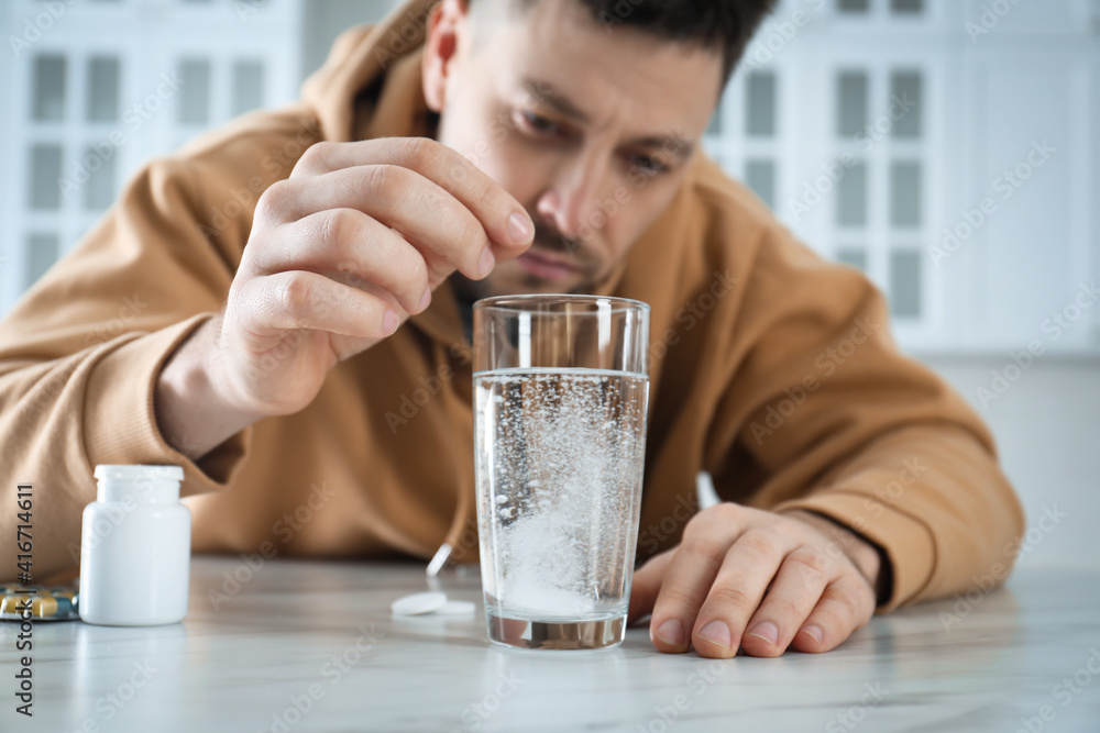 Man taking medicine for hangover at table in kitchen Man taking medicine for hangover at table in kitchen