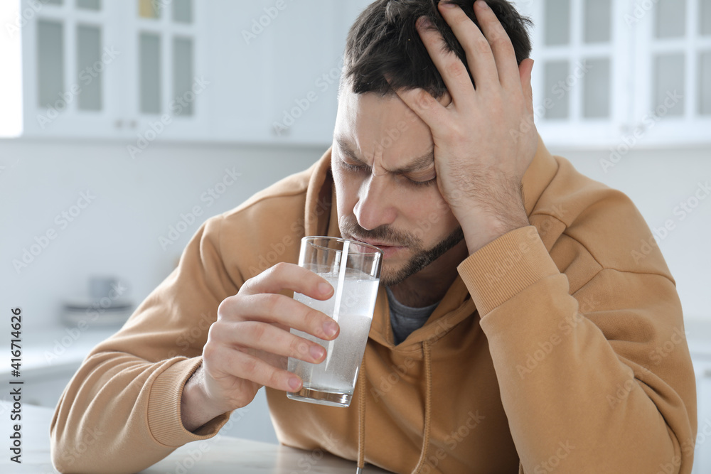 Man taking medicine for hangover at table in kitchen Man taking medicine for hangover at table in kitchen