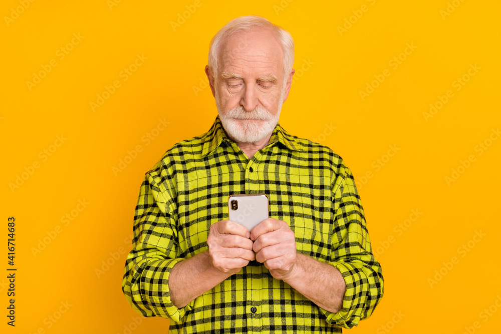 Photo of serious old man grandfather look read browse cellphone isolated over yellow color background Photo of serious old man grandfather look read browse cellphone isolated over yellow color background