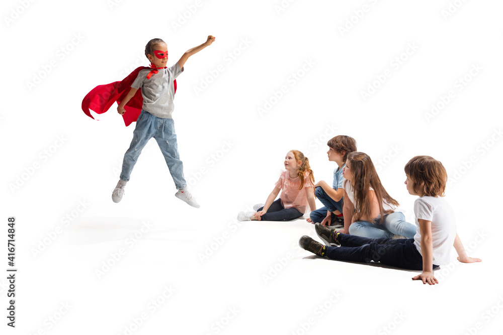Power. Child pretending to be a superhero with her friends sitting ...