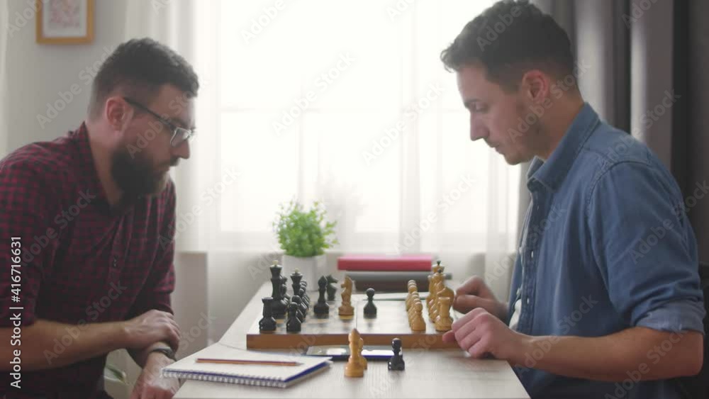 Two young men playing chess at home in the living room Two young men playing chess at home in the living room