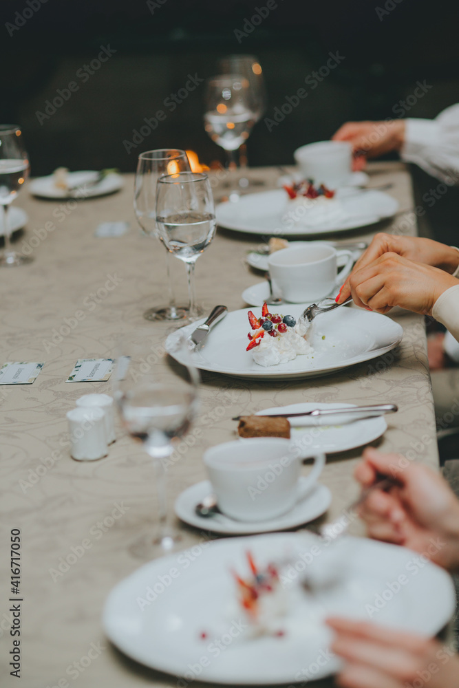Photo of female hands cutting a fruit cake with strawberries, mint and black currants on a white plate on a table in a restaurant. dessert pavlova. table etiquette Photo of female hands cutting a fruit cake with strawberries, mint and black currants on a white plate on a table in a restaurant. dessert pavlova. table etiquette