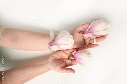 close-up of hand of elderly woman on light background, holding buds of spring flowers, magnolia, concept of awakening of nature, aroma of plants, anti-aging cosmetology and care for aging skin