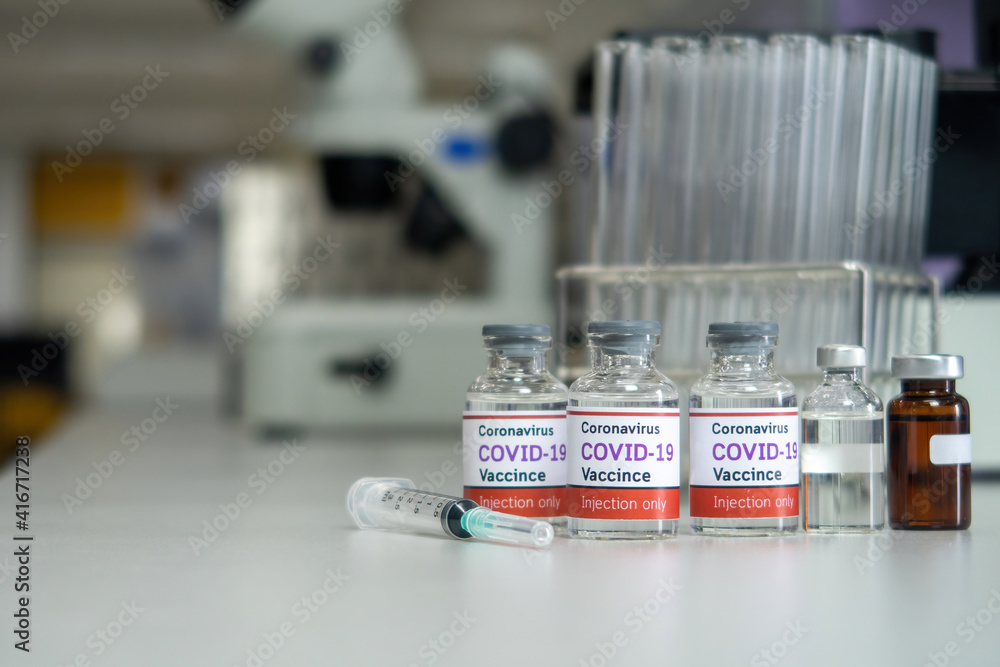Concept of coronavirus vaccine covid-19 vaccine vial with syringe and test tube behind it in medical science lab.