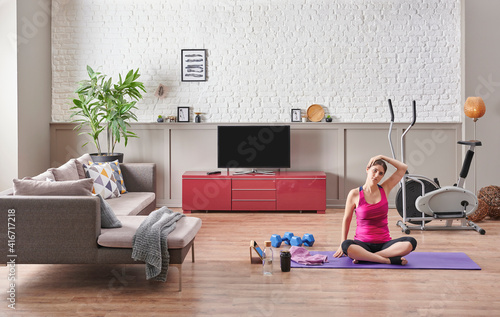 Sportive woman is doing training at home, purple mat, blue dumbbell, decorative living room concept. Healthy lifestyle.