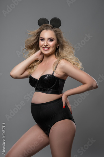 Bild auf Leinwand pregnant girl artistically posing at the camera in a photo studio on a gray back