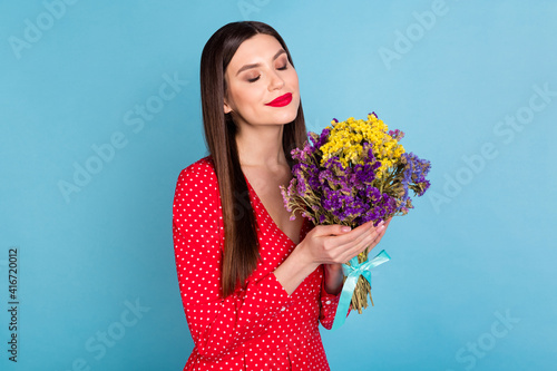 Portrait of attractive cheerful dreamy girl holding in hands smelling blossom flowers isolated over bright blue color background
