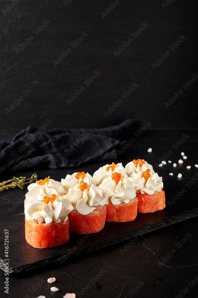 rolls with creamy sauce on a black wooden board on a black textured background rolls with creamy sauce on a black wooden board on a black textured background