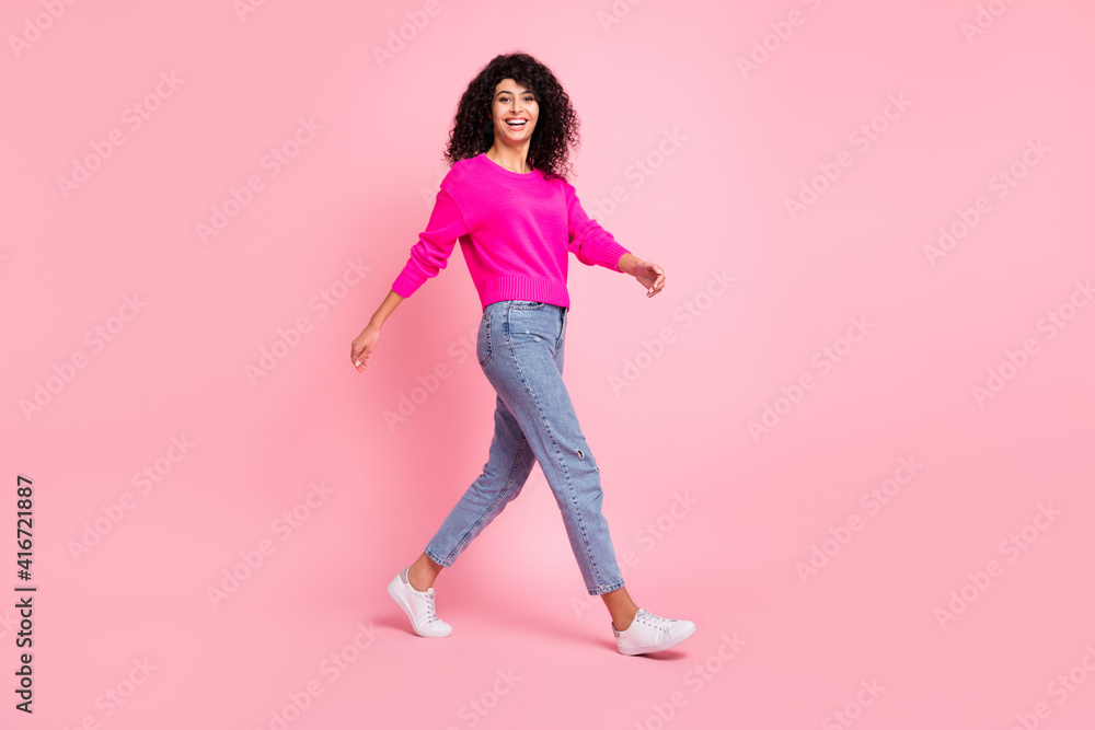 Full size profile side photo of young happy positive attractive girl go walk wear bright jumper isolated on pink color background Full size profile side photo of young happy positive attractive girl go walk wear bright jumper isolated on pink color background