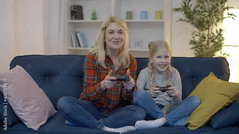 Excited mom and daughter playing video games at home, celebrating victory, fun Excited mom and daughter playing video games at home, celebrating victory, fun