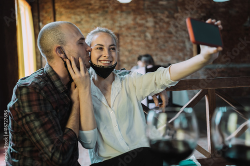 The happy couple wearing protective masks take a selfie in the restaurant.