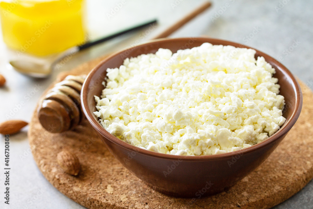 Rich in calcium healthy food. Tvorog, farmers cheese, curd cheese or cottage cheese in a bowl with honey and almond on stone table. Rich in calcium healthy food. Tvorog, farmers cheese, curd cheese or cottage cheese in a bowl with honey and almond on stone table.