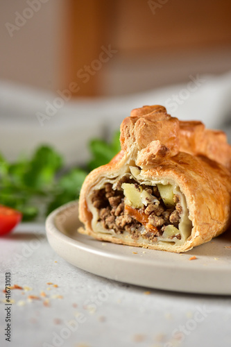 English pie with minced meat and vegetables, cutaway on a gray plate.