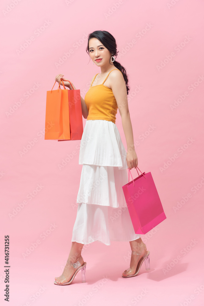 Full length portrait of a beautiful young woman posing with shopping bags, isolated against pink background