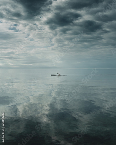 Un ragazzo e la sua canoa in mezzo al mare con un cielo immenso