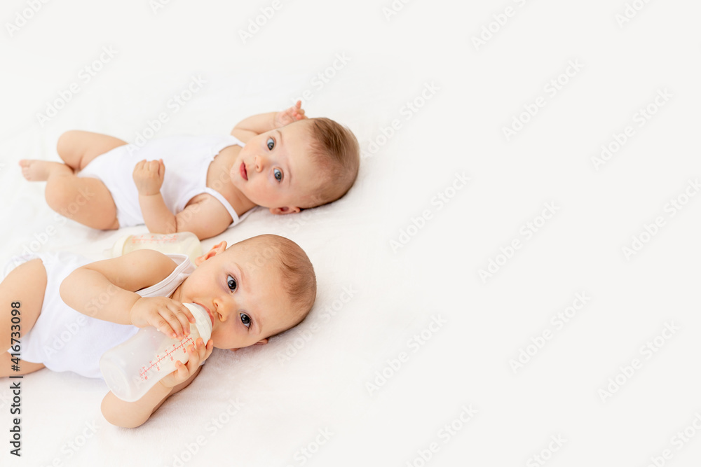 twin babies boy and girl with a bottle of milk on a white bed at home, baby food concept, place for text twin babies boy and girl with a bottle of milk on a white bed at home, baby food concept, place for text