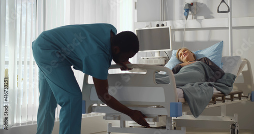 Afro-american man nurse adjusting bed for woman patient