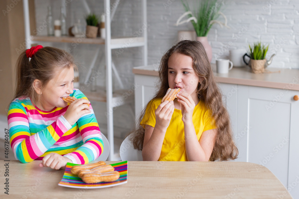 Portrait of two teenage beautiful smiling hipster girls in fashionable clothes. carefree children posing against the backdrop of the kitchen. Positive models have fun with sweets. Portrait of two teenage beautiful smiling hipster girls in fashionable clothes. carefree children posing against the backdrop of the kitchen. Positive models have fun with sweets.