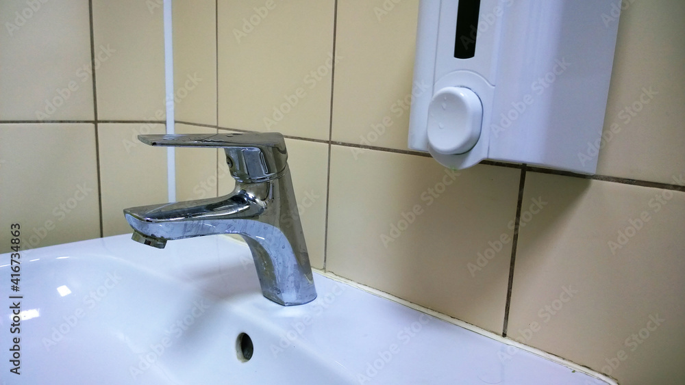Modern white bathroom sink and faucet in public toilet and restroom. Manual tap, hand sanitizer and liquid soap. Virus protection concept. Sanitary rules. Contemporary washroom and wc. Hygiene. Modern white bathroom sink and faucet in public toilet and restroom. Manual tap, hand sanitizer and liquid soap. Virus protection concept. Sanitary rules. Contemporary washroom and wc. Hygiene.